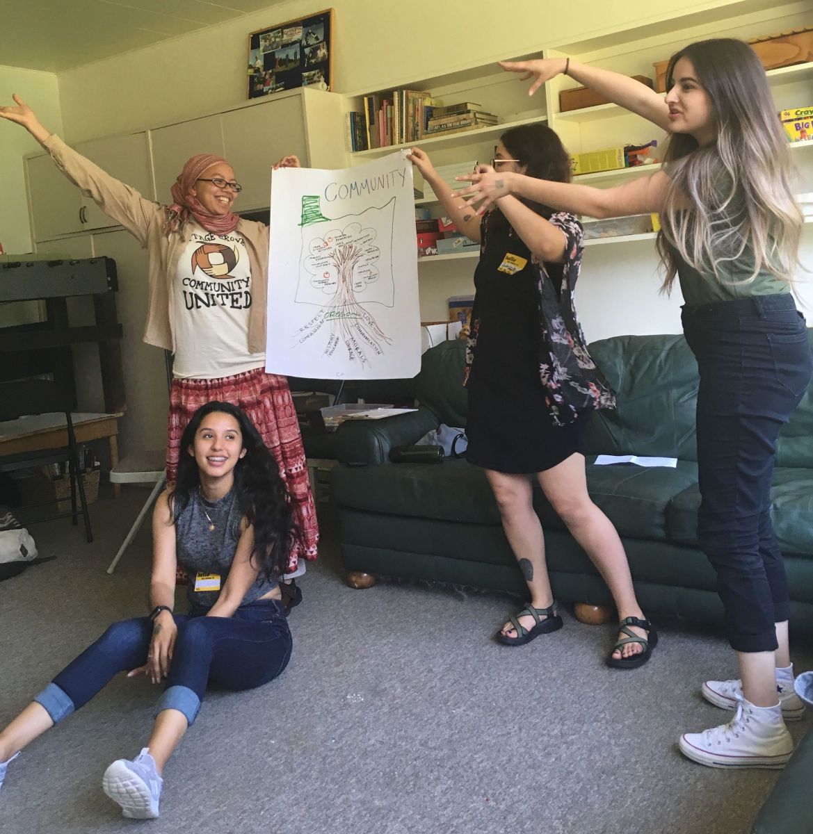four people presenting a flipchart paper with a drawing of a tree and a text that says community.